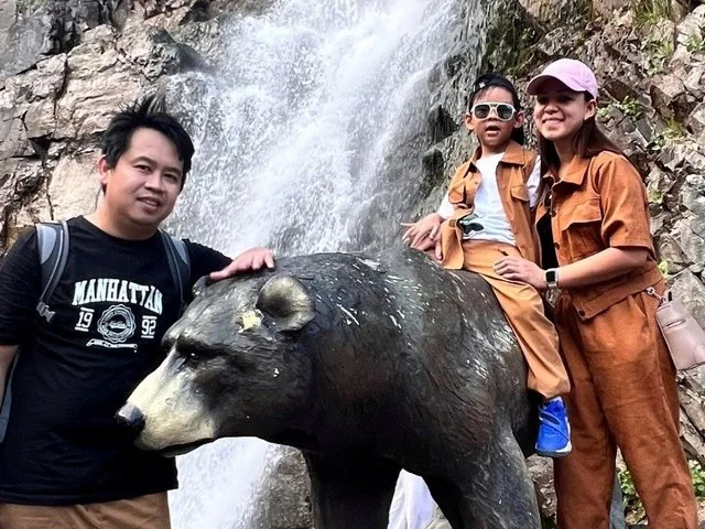 Famiglia in posa accanto a una statua di orso vicino a una cascata al Lago Issyk.