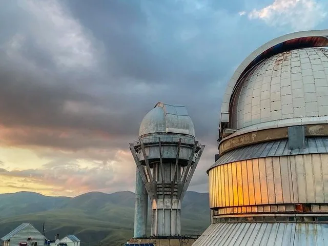 Observatoriumskuppeln auf dem Assy-Plateau unter einem dramatischen, wolkenverhangenen Abendhimmel.