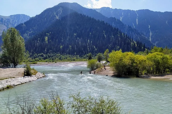 Personas vadeando un río poco profundo que desemboca en un lago de montaña.